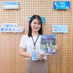 微笑的会议与会者在品牌公司展示墙前手持家庭旅行宣传册。