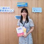 身穿花裙的女子站在品牌背景墙前,手里拿着两本彩色书