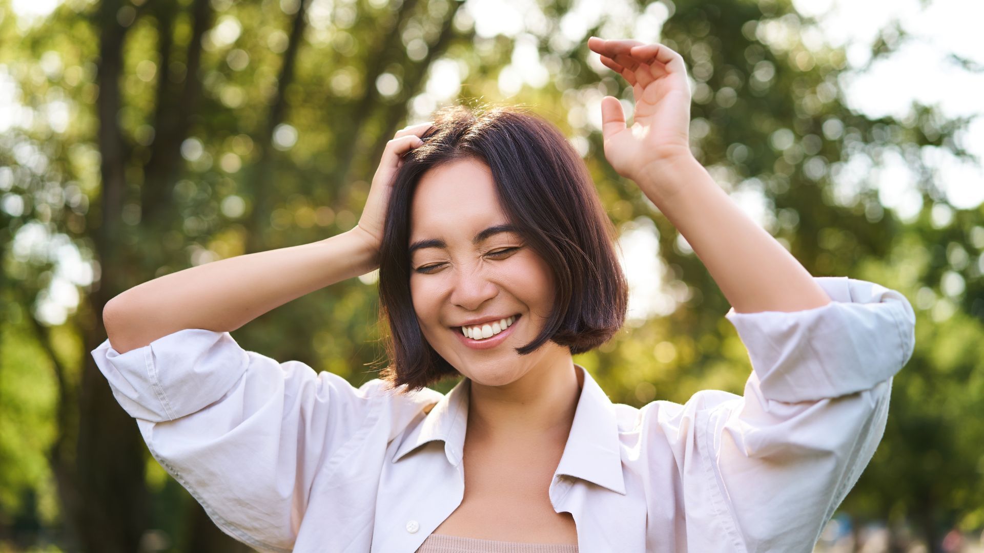 一位面带微笑的女子置身于大自然中，双眼紧闭，双手高举。